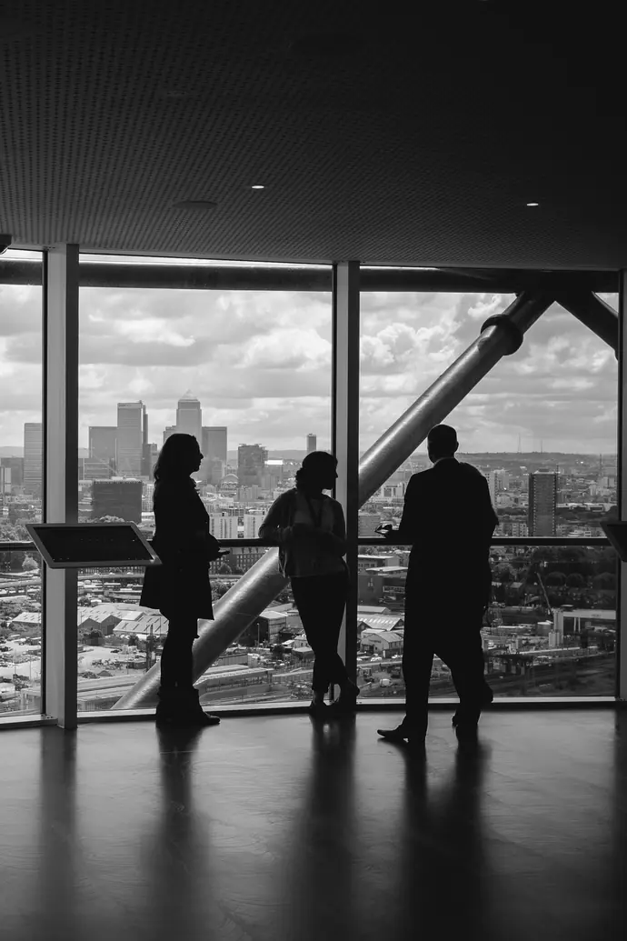 Drei Geschäftsleute im Gespräch vor einer Fensterfront mit Blick auf die Skyline