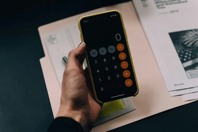 Hand mit Smartphone-Taschenrechner über Rechnungsunterlagen